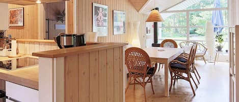 A kitchen with wooden paneling, a dining area with wicker chairs, and a large window providing natural light.