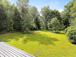 A grassy outdoor area with a wooden deck, surrounded by dense trees. - Holiday Home in Vejby (Vejby)