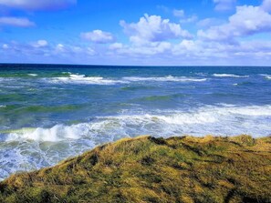 A coastal landscape with waves crashing onto the shore, a clear sky, and a grassy cliff. - Holiday Home in Vejby (Vejby)