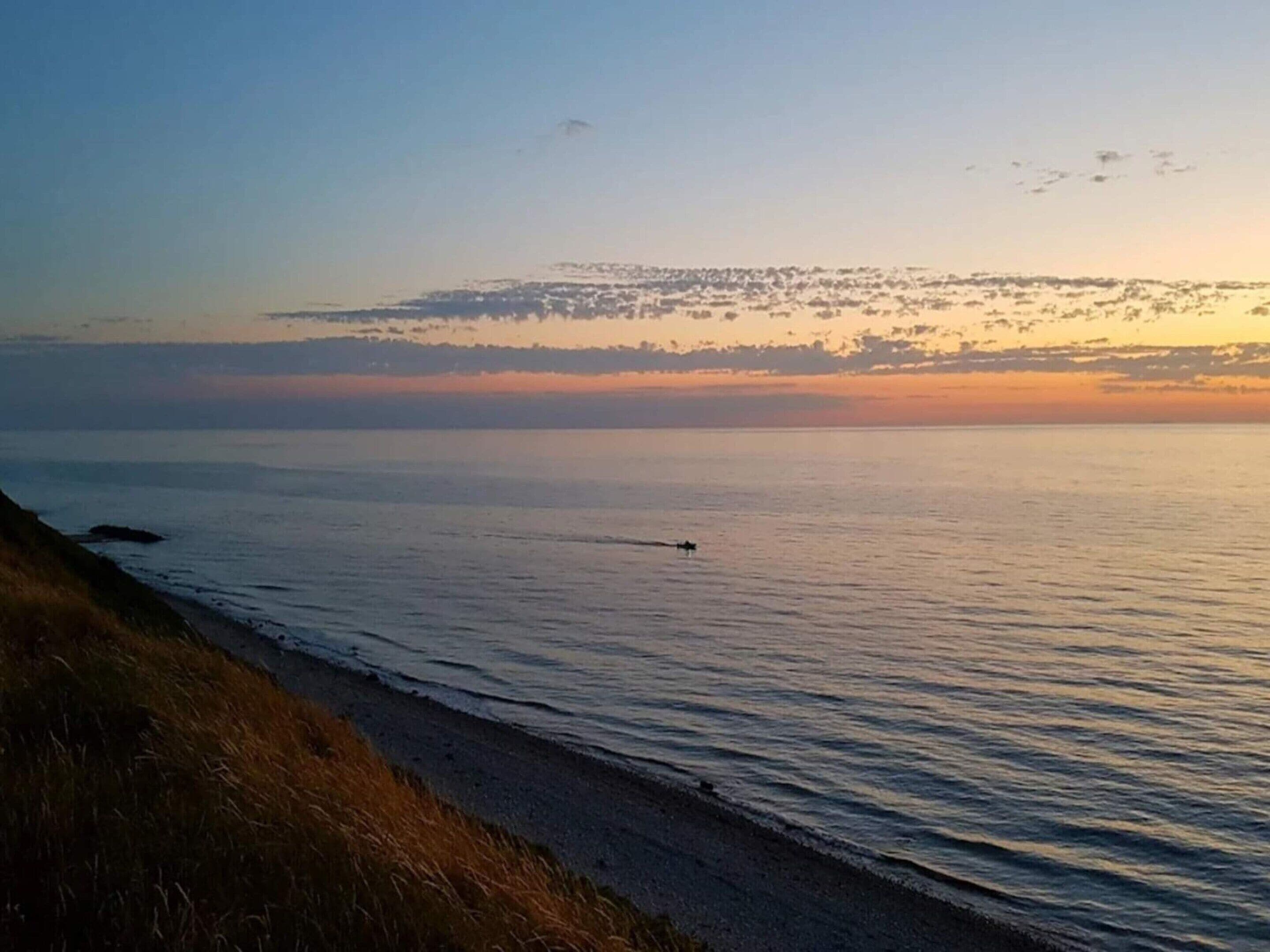 Platja amb cel blau, mar tranquil·la i una costa llunyana.