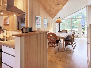 A kitchen with wooden paneling, a dining area with wicker chairs, and a large window providing natural light. - Holiday Home in Vejby (Vejby)