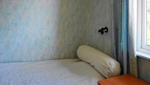 Una habitación pequeña con una cama individual, una mesita de noche de madera, una ventana con cortinas y un muro con garabatos.