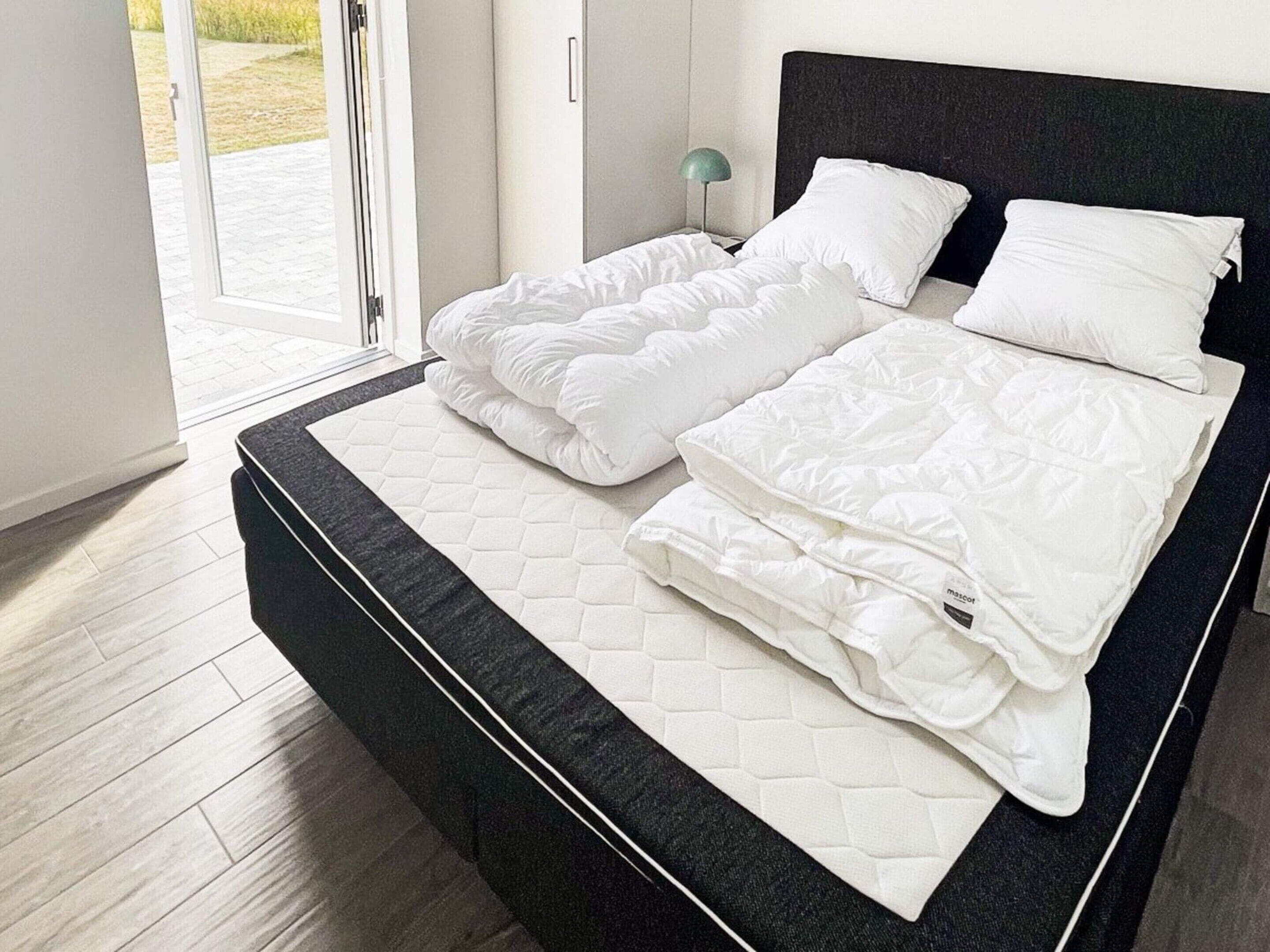 A modern bedroom with a large bed, a nightstand, and a view of the outdoors through a glass door.