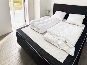 A modern bedroom with a large bed, a nightstand, and a view of the outdoors through a glass door. - Holiday Home in Dannemare (Dannemare)