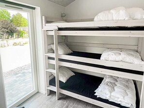 A bunk bed with white bedding in a room with a view of a paved area and trees. - Holiday Home in Dannemare (Dannemare)