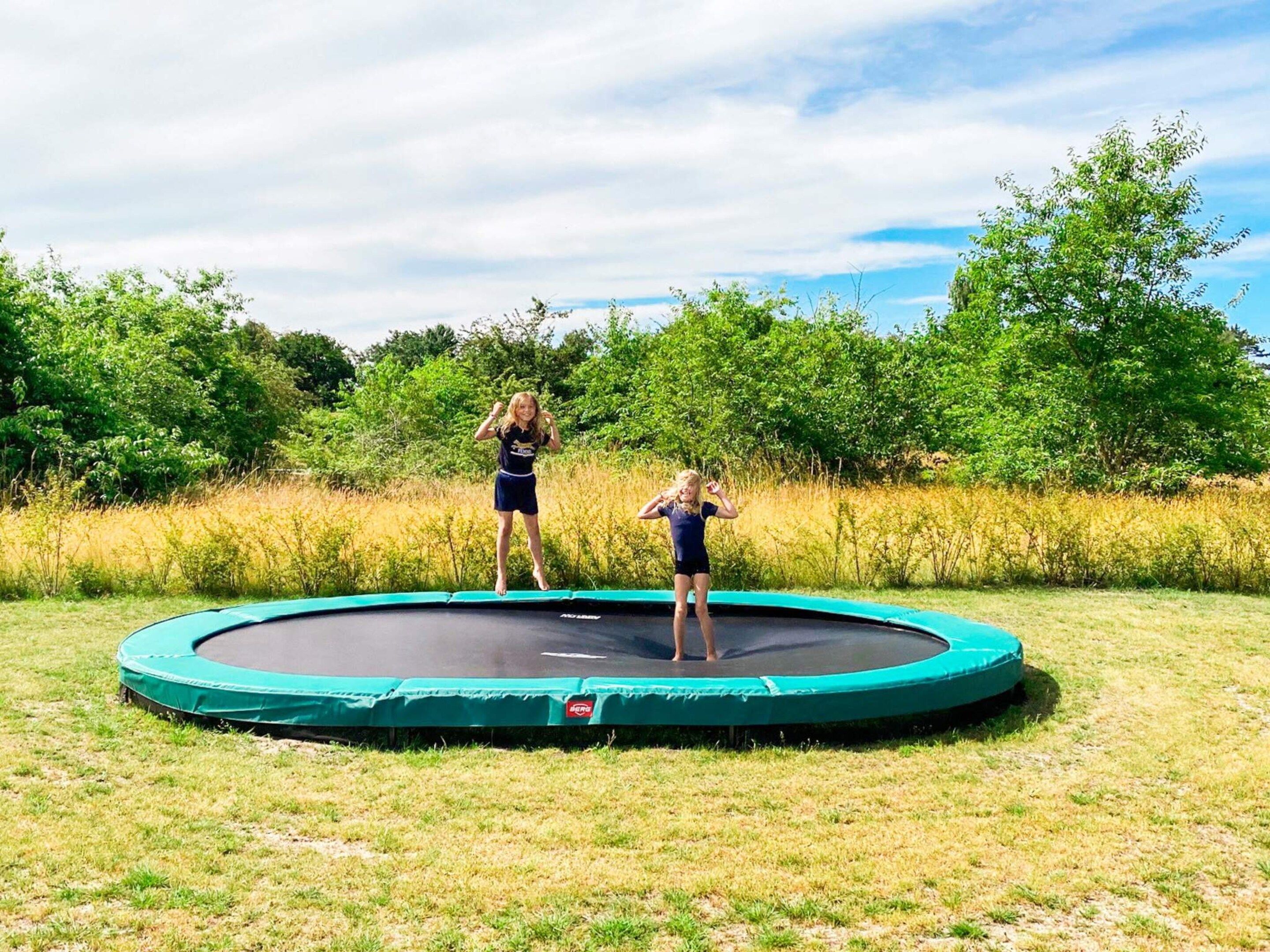 A trampoline in a grassy area with trees in the background.