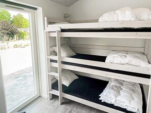 A bunk bed with white bedding in a room with a view of a paved area and trees.