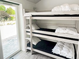 Una cama litera con ropa de cama blanca en una habitación con vistas a un área pavimentada y árboles.