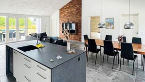 A modern kitchen with a central island, built-in cabinets, and a dining area with a table and chairs. - Holiday Home in Dannemare (Dannemare)