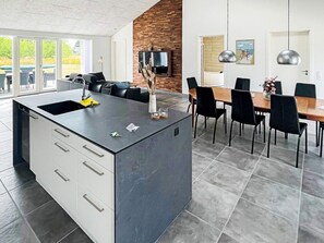 A modern kitchen with a central island, built-in cabinets, and a dining area with a table and chairs. - Holiday Home in Dannemare (Dannemare)