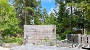 A wooden deck with a table and chairs, surrounded by a rustic fence and greenery.