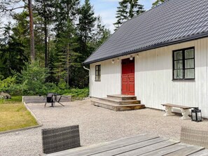 Un bâtiment blanc avec une porte rouge, une terrasse en bois et un banc.