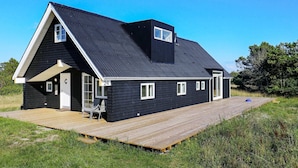 A black single-story house with a wooden deck, a small porch, and a chimney. - Holiday Home in Skagen (Skagen)