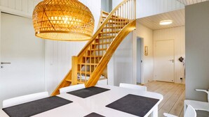 A modern interior with a wooden staircase, white walls, and a dining area with black placemats. - Holiday Home in Skagen (Skagen)