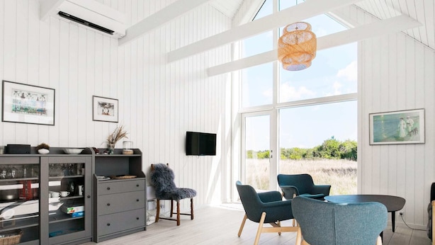 A modern living room with a dining area, featuring a large window, a TV, and a cozy chair. - Holiday Home in Skagen (Skagen)