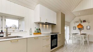 A modern kitchen with white cabinetry, a built-in oven, and a window above the sink. - Holiday Home in Skagen (Skagen)