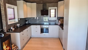Uma cozinha moderna com armários brancos, forno embutido e lareira a lenha.