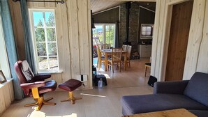 Uma sala de estar acolhedora com um sofá, uma poltrona, uma mesa de centro de madeira e um espaço de jantar com mesa e cadeiras.