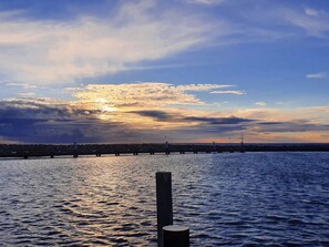 A waterfront view with a pier extending into the water, a clear sky, and a sunset.
