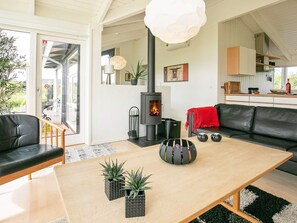 Una sala de estar moderna con chimenea, sofá de cuero negro, mesa de centro de madera y plantas en macetas.