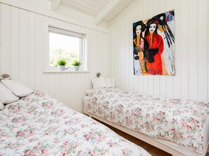 A bedroom with two beds, a window with plants, and a painting on the wall.