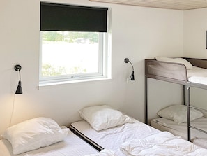 A dormitory room with bunk beds, a window with a black blind, and two wall-mounted reading lamps.