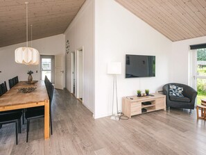 A modern living room with a wooden dining table, a flat-screen TV, and a comfortable seating area. - Holiday Home in Ansager (Ansager)