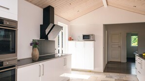 A modern kitchen with white cabinetry, a built-in oven, and a microwave on the countertop. - Holiday Home in Ansager (Ansager)