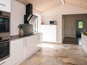 A modern kitchen with white cabinetry, a built-in oven, and a microwave on the countertop. - Holiday Home in Ansager (Ansager)