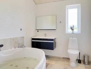 A bathroom with a bathtub, a toilet, a sink, and a window with a view. - Holiday Home in Ansager (Ansager)