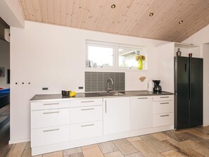 A modern kitchen with white cabinetry, a stainless steel refrigerator, and a window above the sink. - Holiday Home in Ansager (Ansager)
