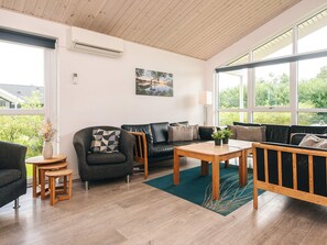A modern living room with a sofa, armchair, coffee table, and a view of greenery outside. - Holiday Home in Ansager (Ansager)