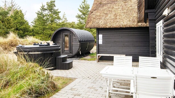Una cabaña con techo de paja, jacuzzi y terraza de madera.