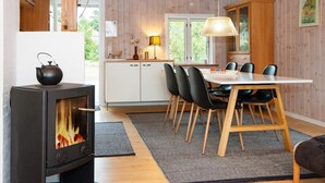 Una cocina acogedora con armarios de madera, una mesa de comedor con sillas, una estufa negra y una lámpara colgante.
