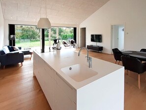 Una cucina moderna con un'isola grande, un'area pranzo con tavolo e sedie, una TV montata a parete e vista sull'esterno.