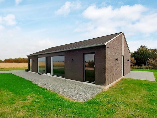 Un bâtiment moderne doté d’un toit en pente, de grandes portes vitrées et d’un chemin de gravier menant à l’entrée.