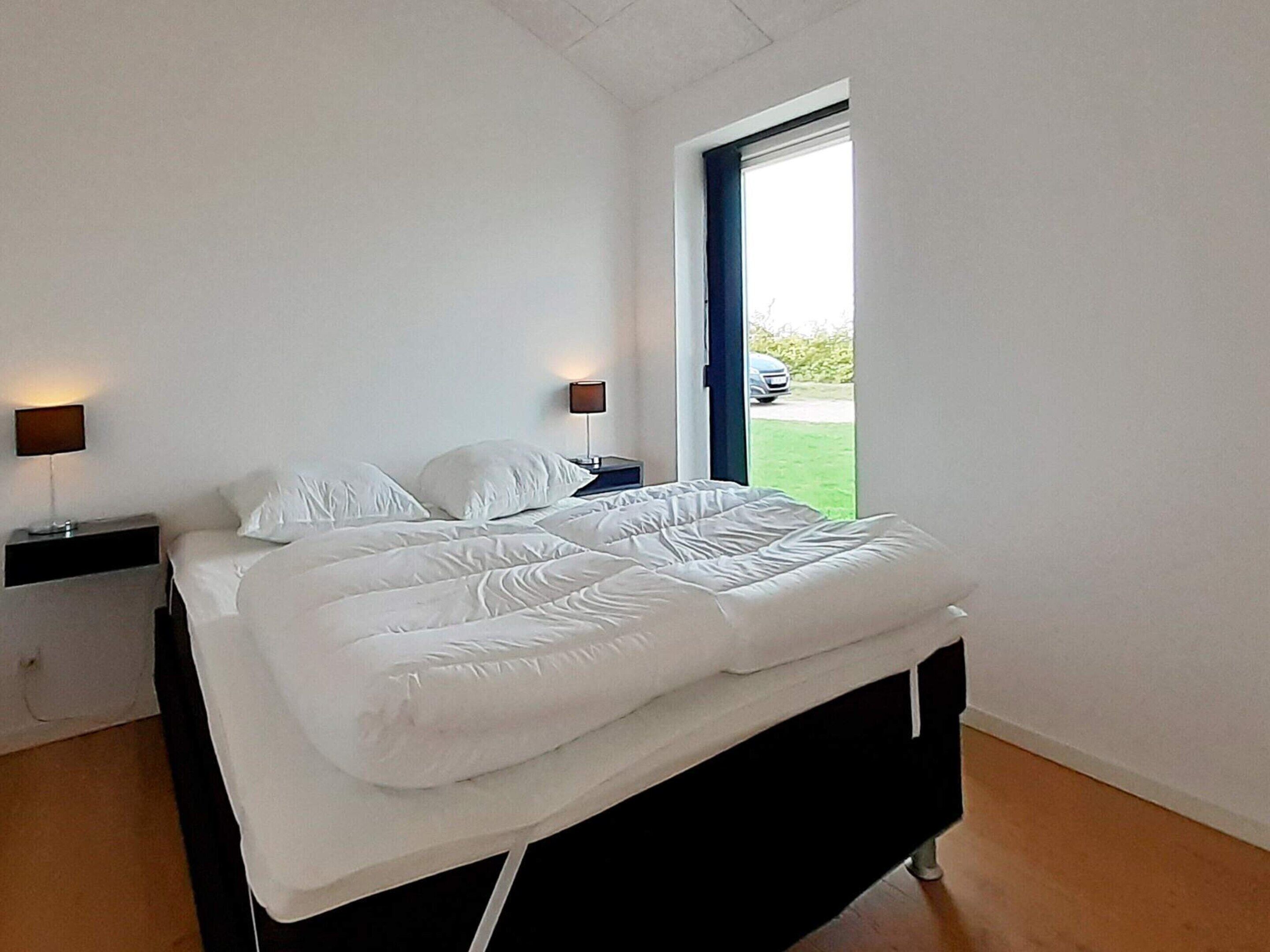 A modern bedroom with a bed, two bedside tables, a window, and a view of the outdoors.