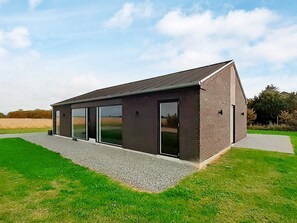 A modern building with a sloped roof, large sliding glass doors, and a gravel pathway leading to the entrance.