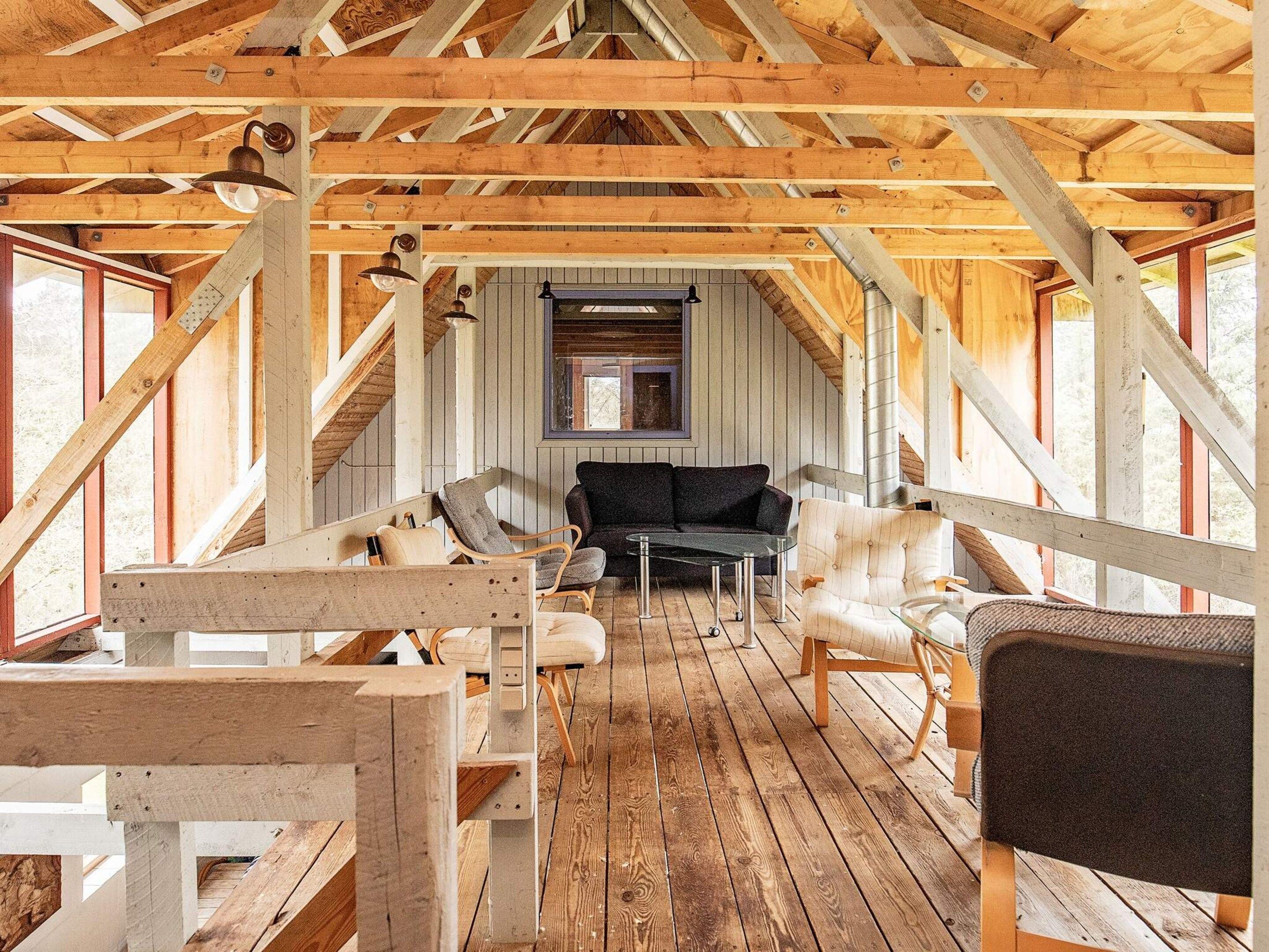Un dormitorio en el ático con vigas de madera, un sofá negro y una mesa de comedor.