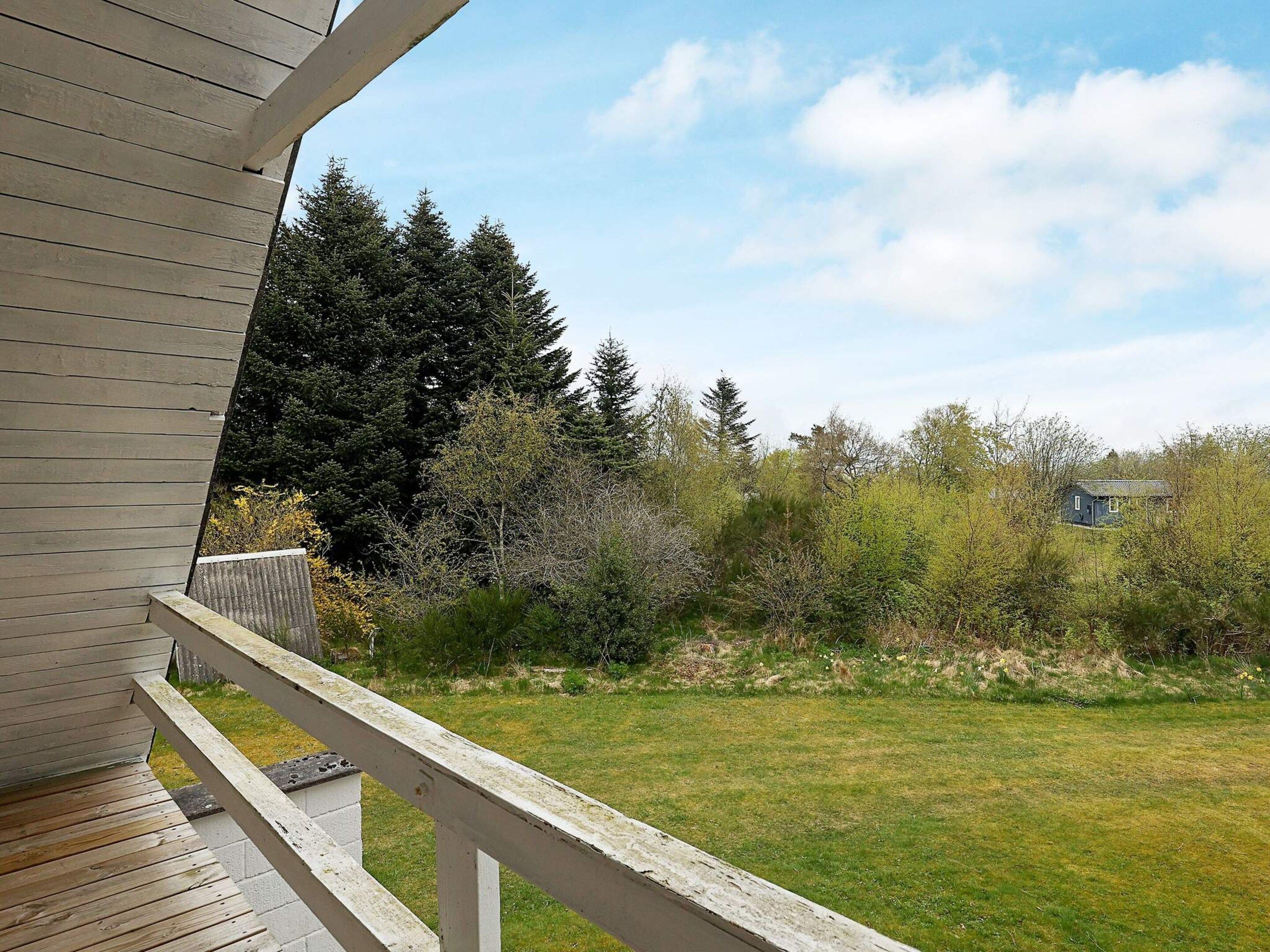 A wooden deck with a railing, a grassy yard, and a house in the background.