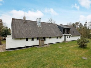 A white building with a sloped roof and a chimney, surrounded by a grassy area and trees.