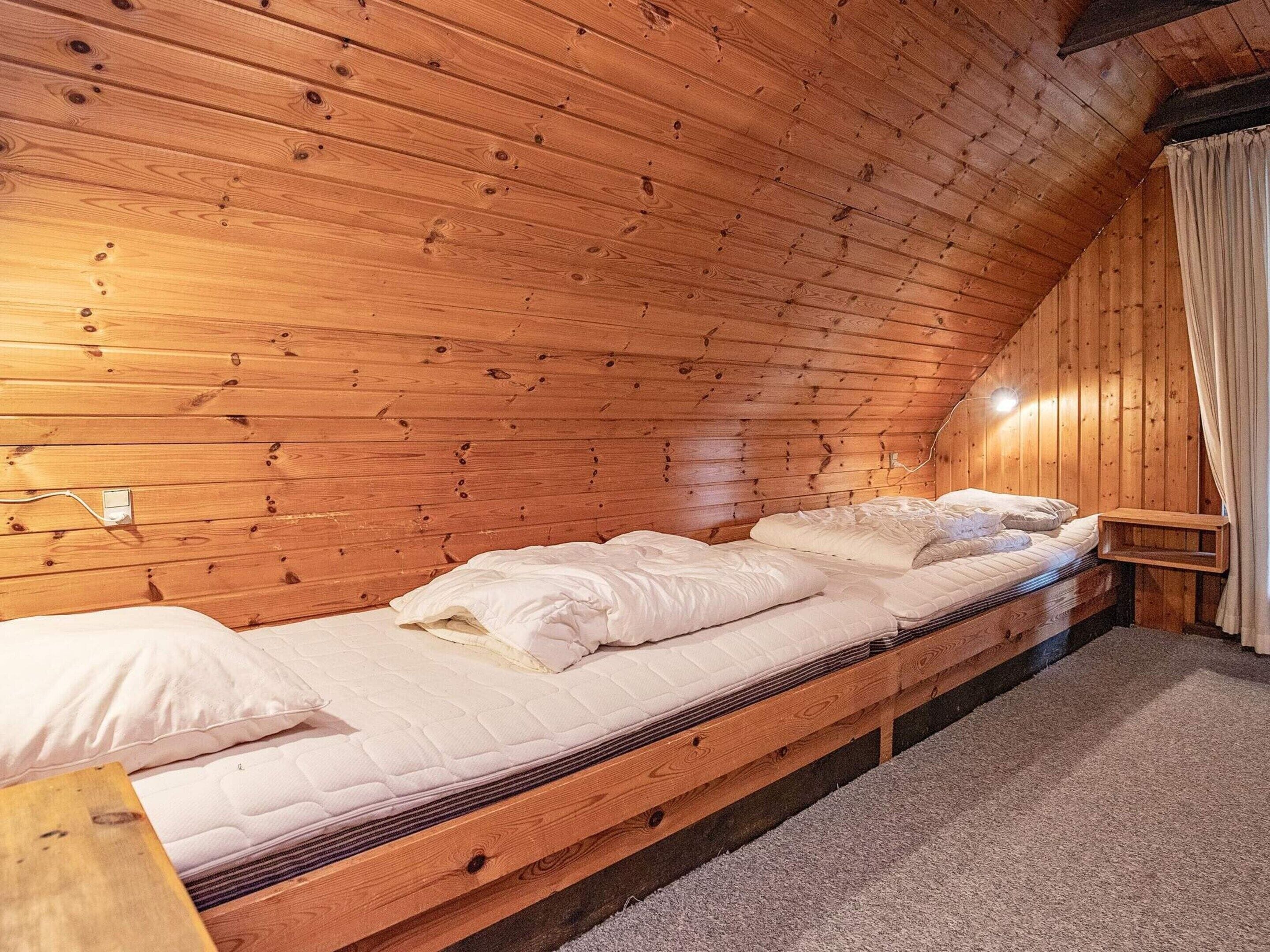 Una cama de madera individual en una habitación tipo cabaña, con techo inclinado y una mesita de noche.
