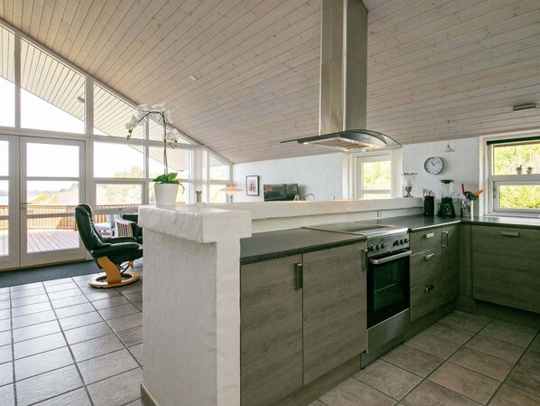 A modern kitchen with a central island, large windows, and a view of the outdoors.