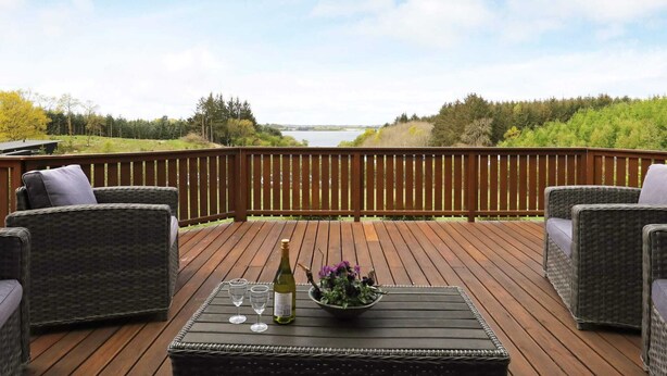 A deck with wicker furniture and a table with a bottle and glasses. - Holiday Home in Skals (Skals)