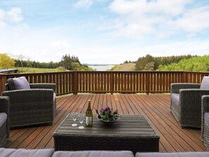 A deck with wicker furniture and a table with a bottle and glasses.