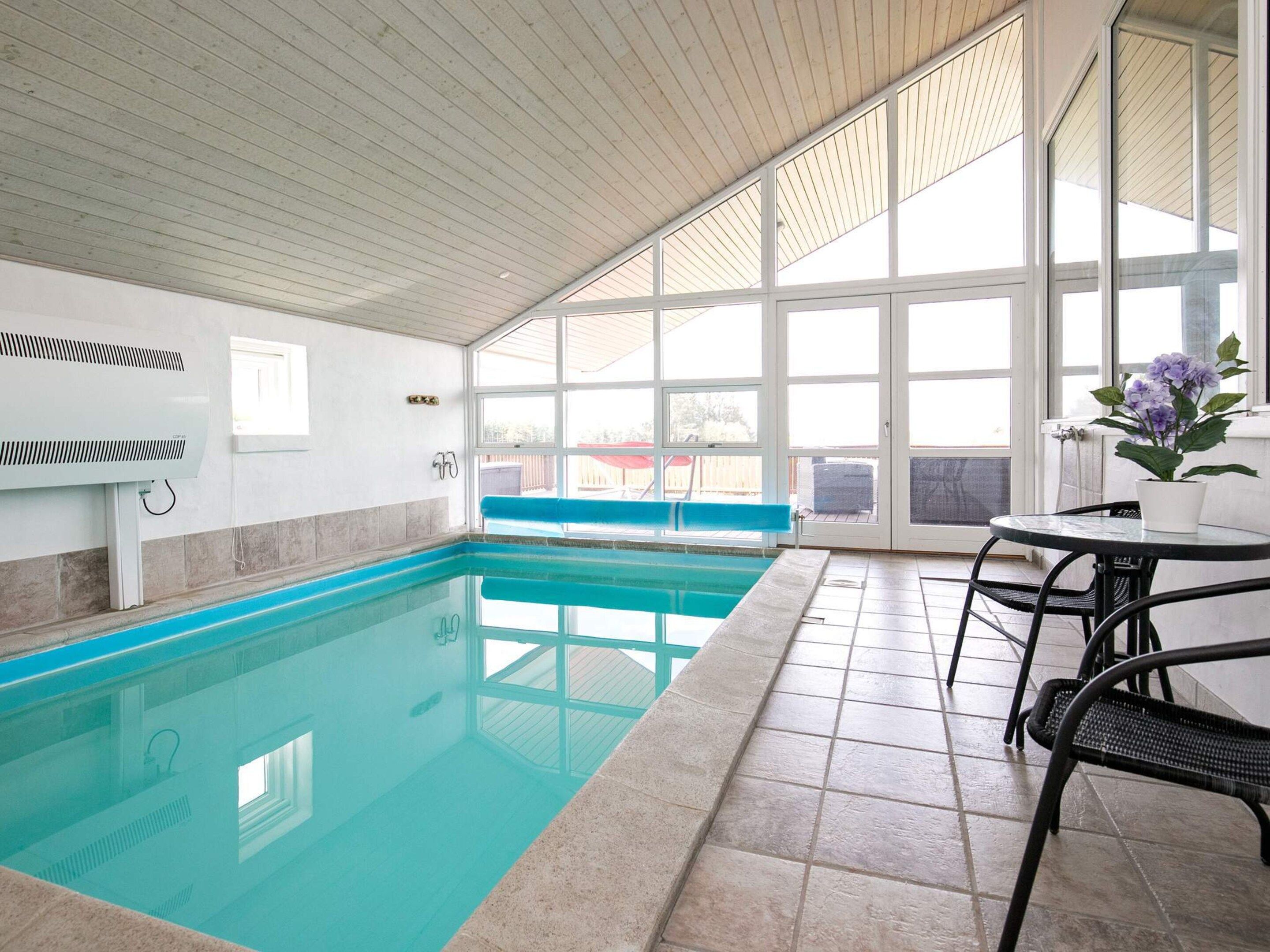 En indendørs swimmingpool med flisegulv, en bænk og et bord med stole.
