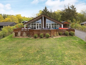 A modern house with a large deck, a covered patio, and a view of a forested area.