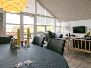 Un espace repas moderne avec une table dressée pour deux personnes, un téléviseur et une vue sur l’extérieur.