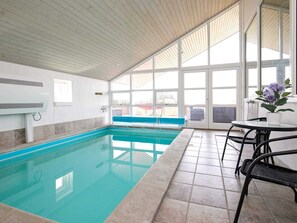An indoor swimming pool with clear glass walls, a blue bench, and a table with chairs. - Holiday Home in Skals (Skals)