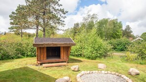 A wooden cabin with a porch, surrounded by a stone fire pit and large rocks.